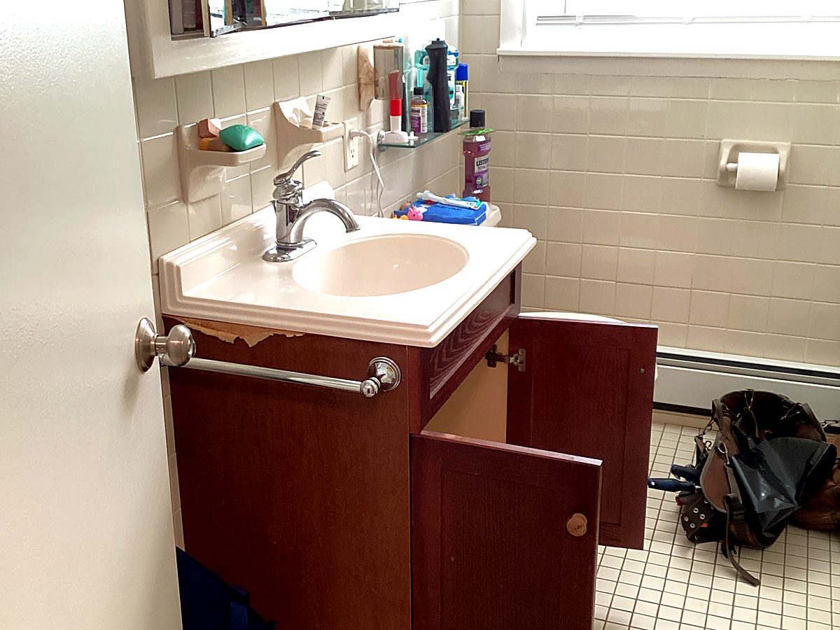 Worn bathroom vanity with peeling laminate before remodel